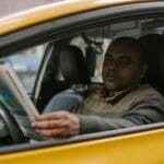 Kierowca taxi w samochodzie czyta magazyn, czekając na pasażera