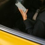 Kobieta w żółtej taksówce patrzy w telefon z aplikacją mapy