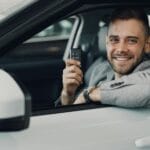 Młody mężczyzna w samochodzie pokazuje kluczyki do świeżo kupionego auta