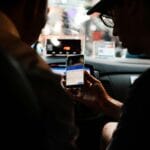 Dwie osoby w nocnym aucie patrzą w smartfon z aplikacją taxi