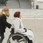 Dziewczynka pcha kobietę na wózku inwalidzkim po kamiennym chodniku