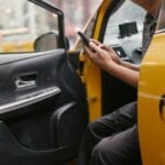 Kierowca taksówki w żółtym aucie płaci smartfonem w mieście