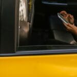 Pasażer na tylnym siedzeniu żółtej taksówki korzysta ze smartfona
