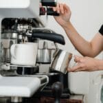 Baristka w fartuchu spienia mleko przy nowoczesnym ekspresie
