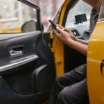 Kierowca żółtej taksówki sprawdza smartfon w miejskim ruchu