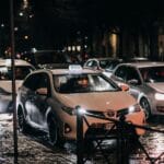 Nocna ulica w deszczu z jadącymi taksówkami i odbiciami świateł