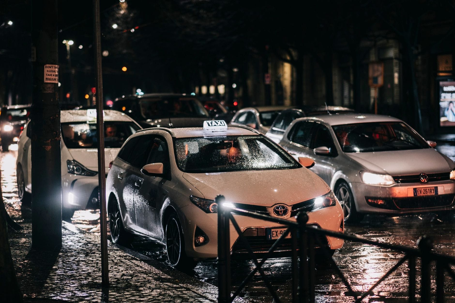 Nocna ulica w deszczu z jadącymi taksówkami i odbiciami świateł